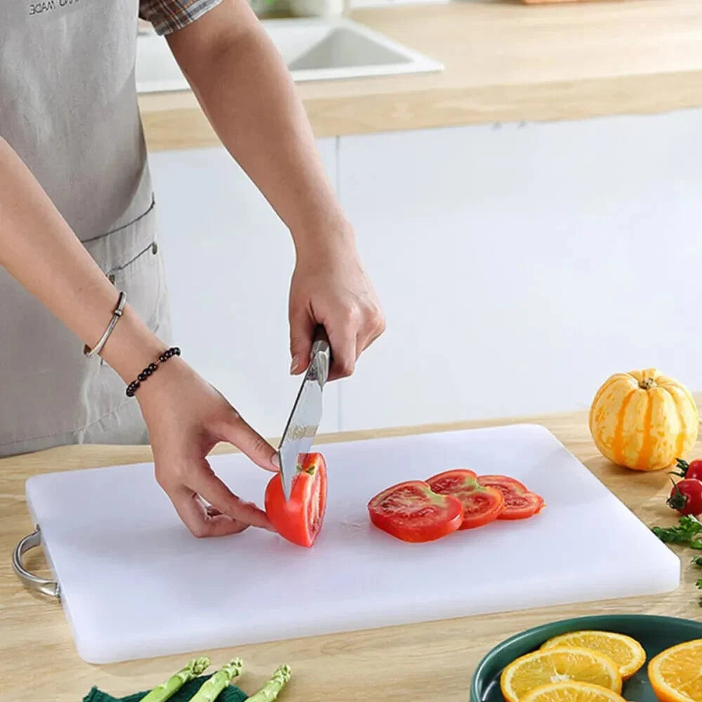 Person slicing red tomato on a thick white plastic cutting board with metal side handle